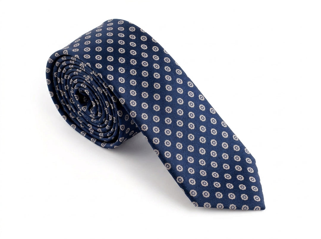A rolled navy blue necktie with a repeating white and light blue geometric pattern, displayed on a clean white background.