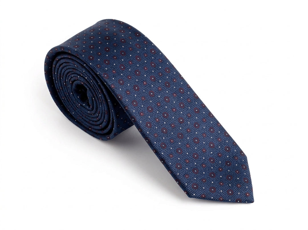 A rolled navy blue silk tie with a small repeating red and white geometric pattern, displayed on a clean white background.