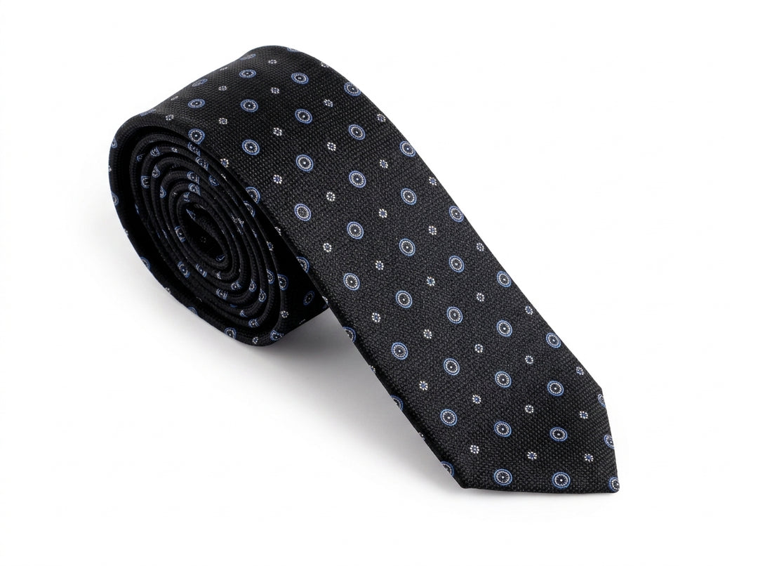 A rolled-up necktie with a black base and a repeating pattern of small blue and white circular motifs, displayed on a clean white background.