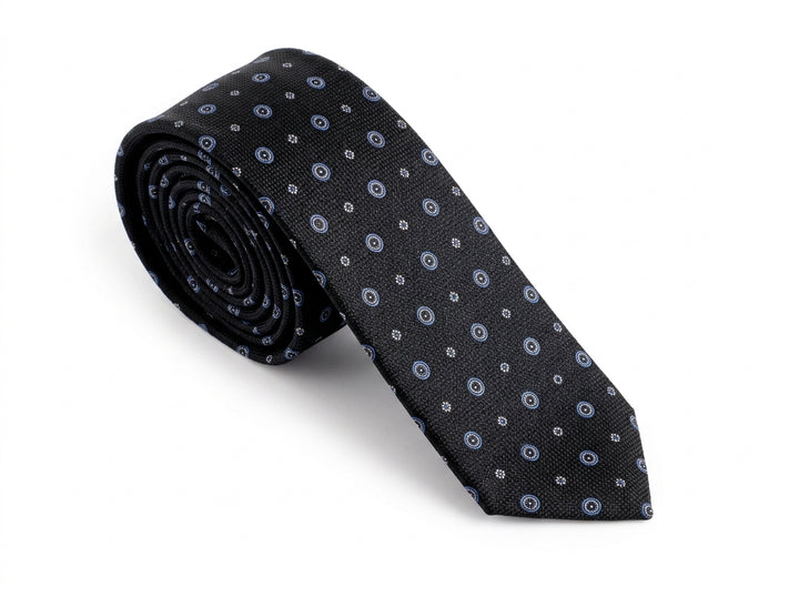 A rolled-up necktie with a black base and a repeating pattern of small blue and white circular motifs, displayed on a clean white background.
