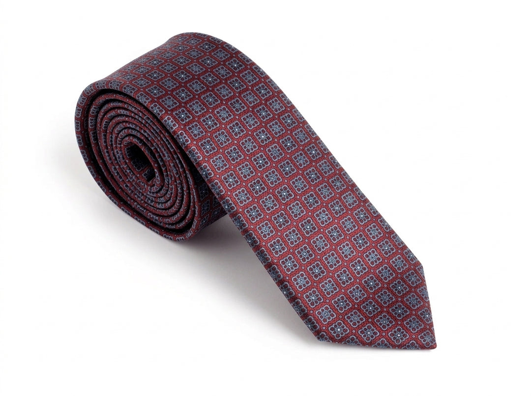 A rolled-up necktie featuring a repeating geometric pattern in burgundy red and blue, displayed on a clean white background.