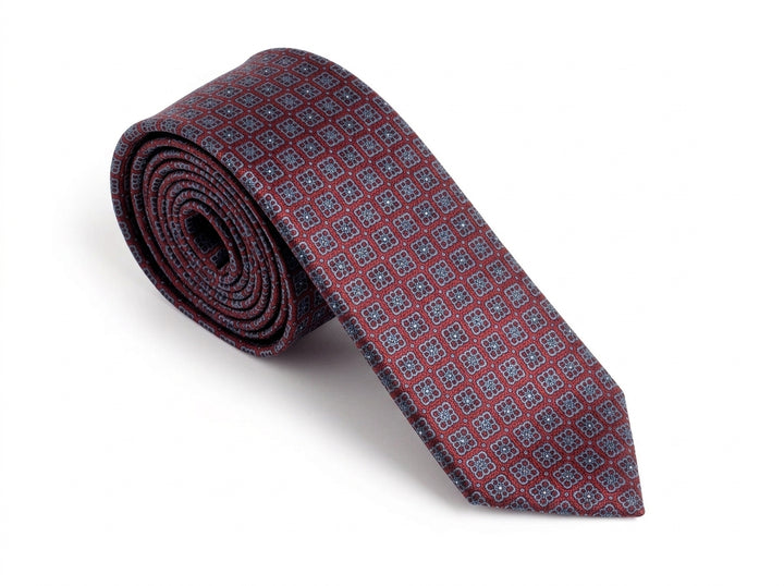 A rolled-up necktie featuring a repeating geometric pattern in burgundy red and blue, displayed on a clean white background.