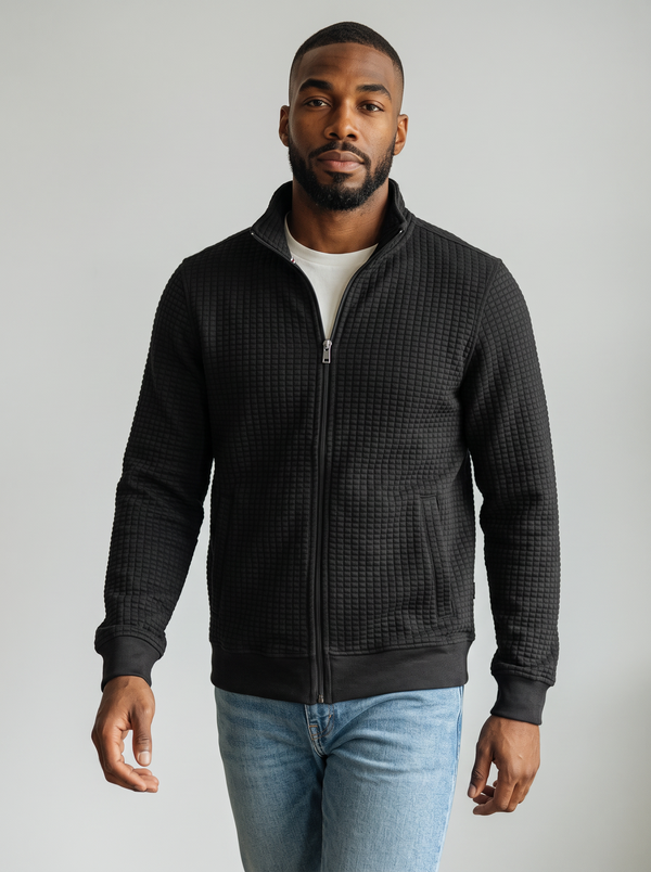 Black jacket with zip closure, stand-up collar, and ribbed cuffs, styled over a white shirt and light blue jeans.