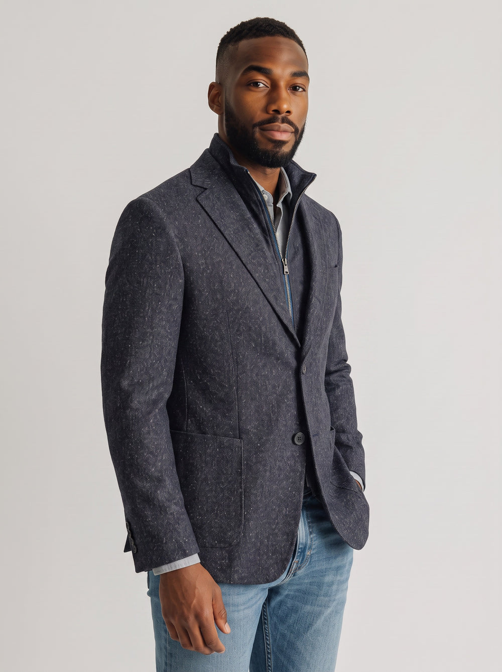 A man wearing a dark gray textured blazer over a collared shirt and blue jeans