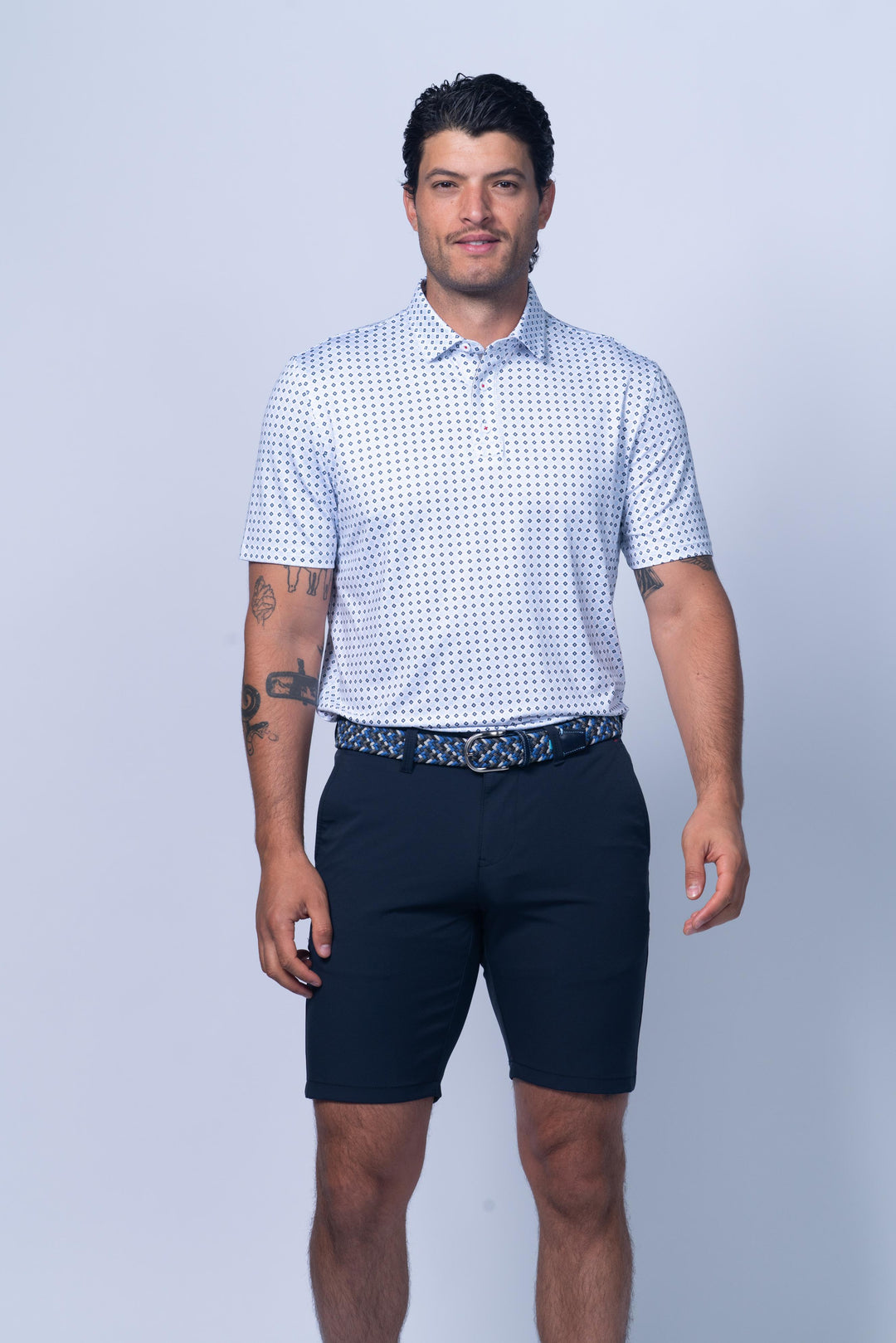 Man wearing a patterned polo shirt and navy shorts on a light gray background