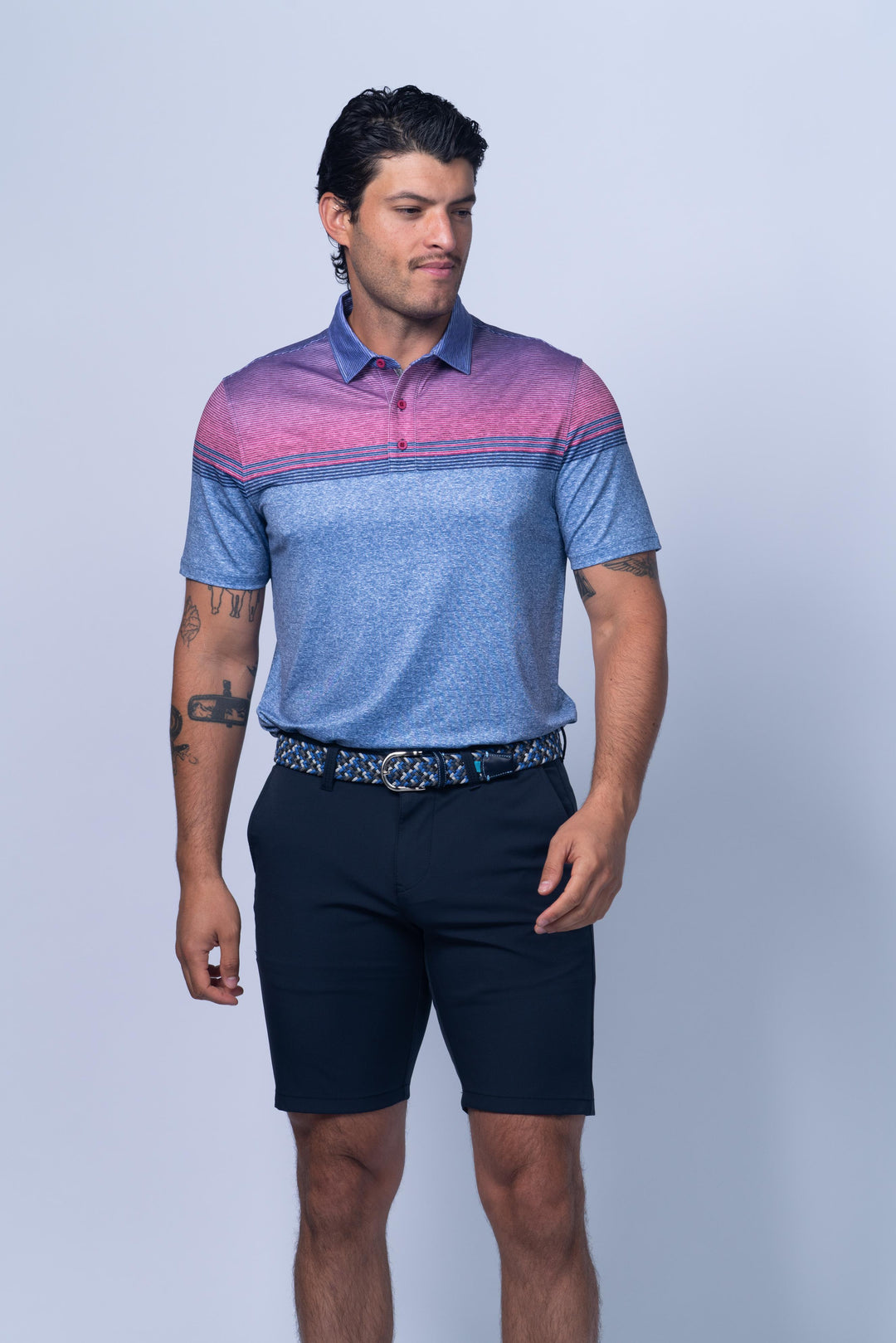 Man wearing a blue and pink striped polo shirt with navy shorts on a light gray background