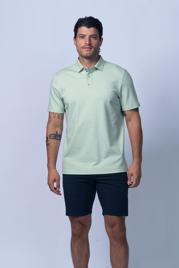 Man wearing a light green polo shirt and navy shorts on a white background