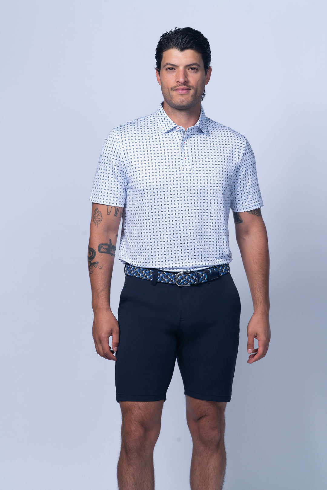 Man wearing a patterned white shirt and navy shorts on a light gray background