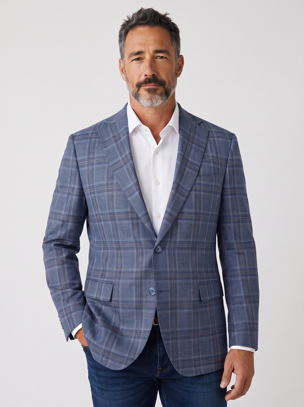 A man wearing a blue plaid blazer over a white dress shirt and blue jeans, standing against a light gray studio background.