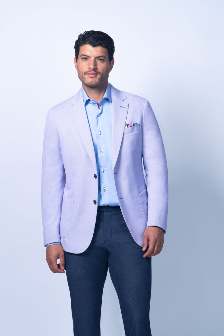 Man wearing a light purple blazer over a blue shirt with dark pants on a white background