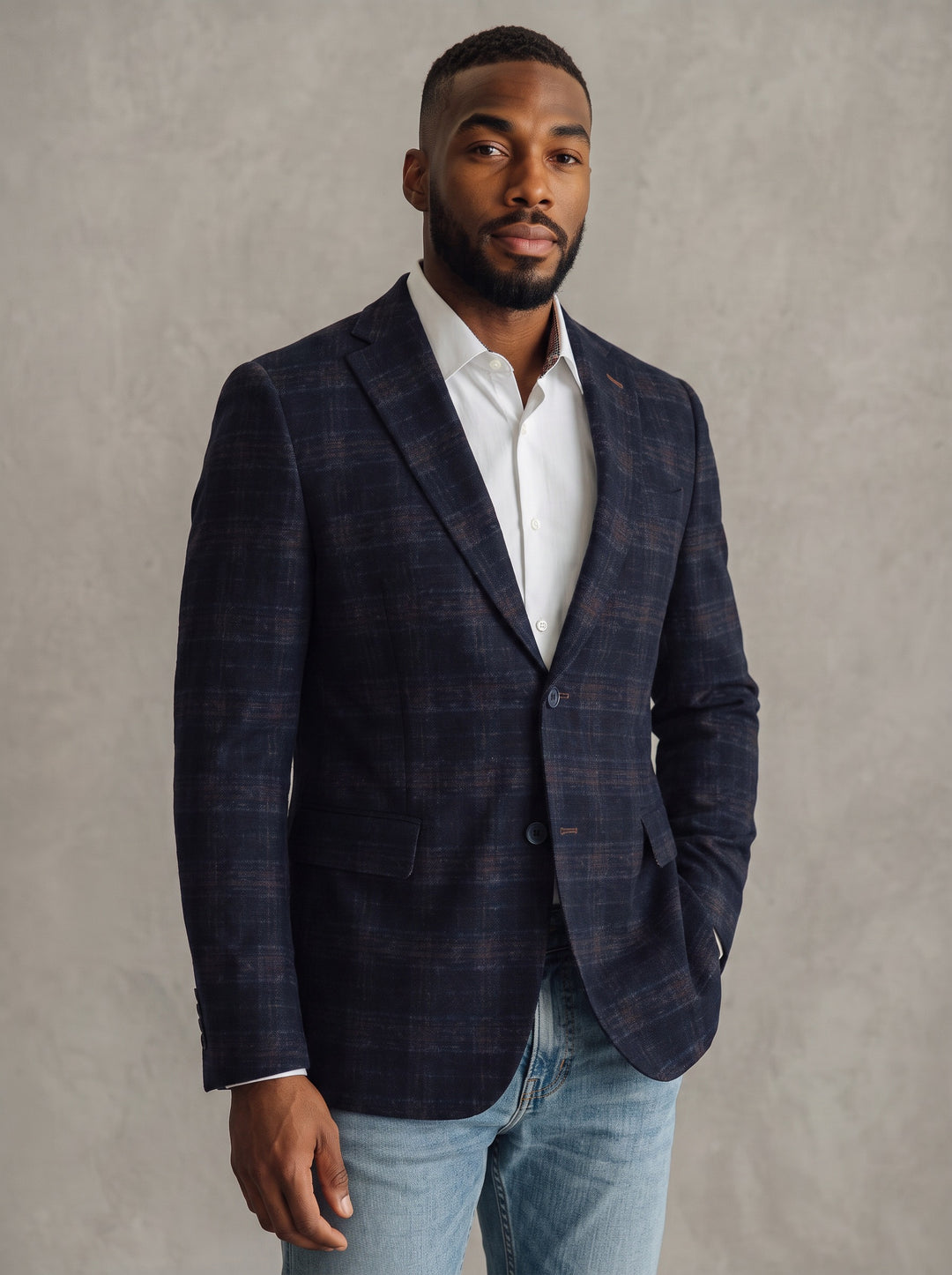 A man wearing a navy blue plaid blazer over a white dress shirt and light blue jeans
