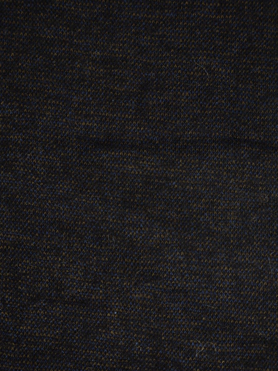 A close-up of a dark woven fabric texture, appearing as a very dark navy or black material with subtle blue and warm brown threads.