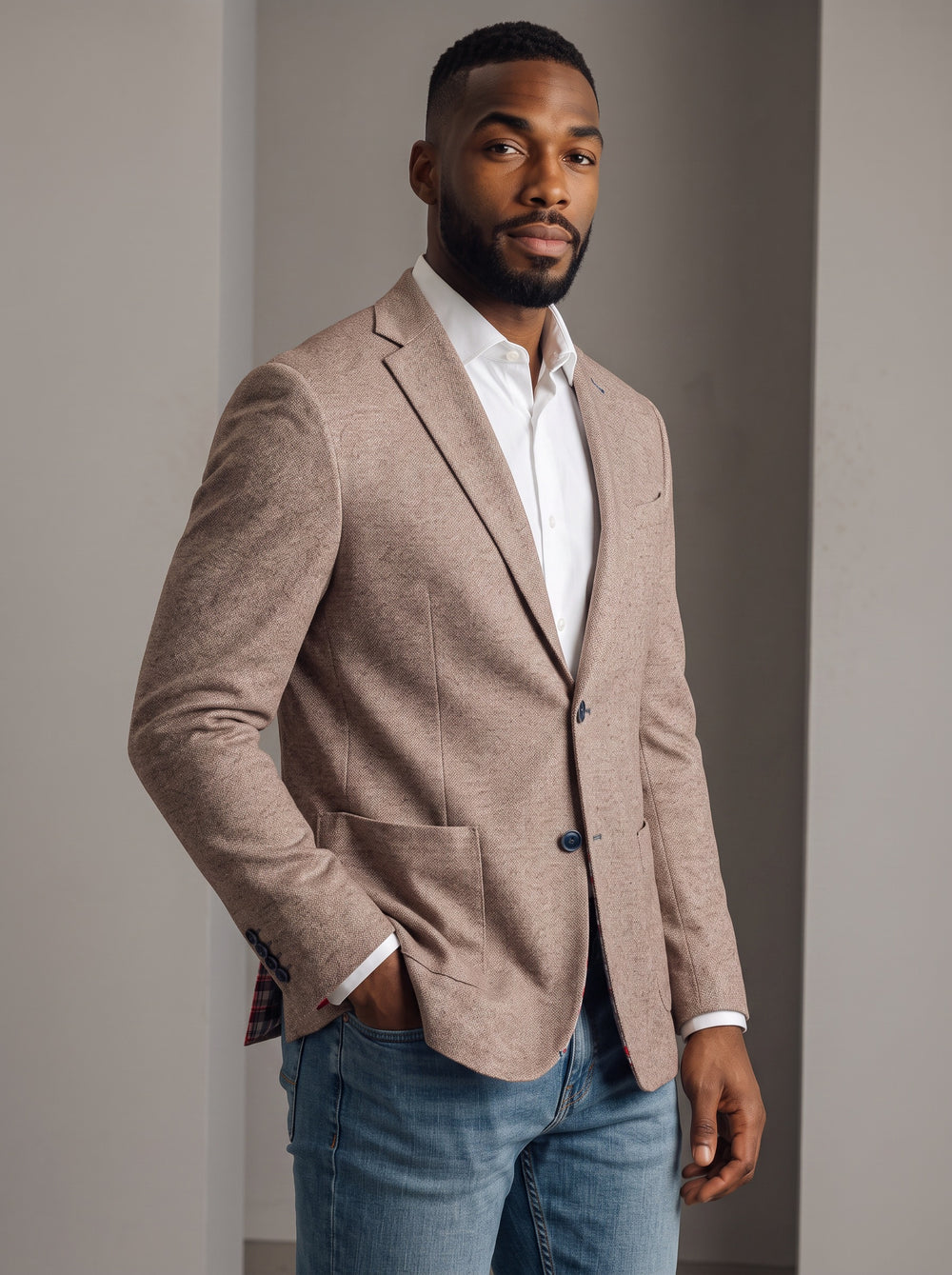 A man wearing a light brown textured blazer over a white dress shirt and blue jeans.