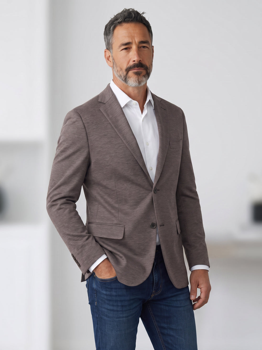 A man wearing a textured taupe-brown blazer over a white dress shirt and blue jeans