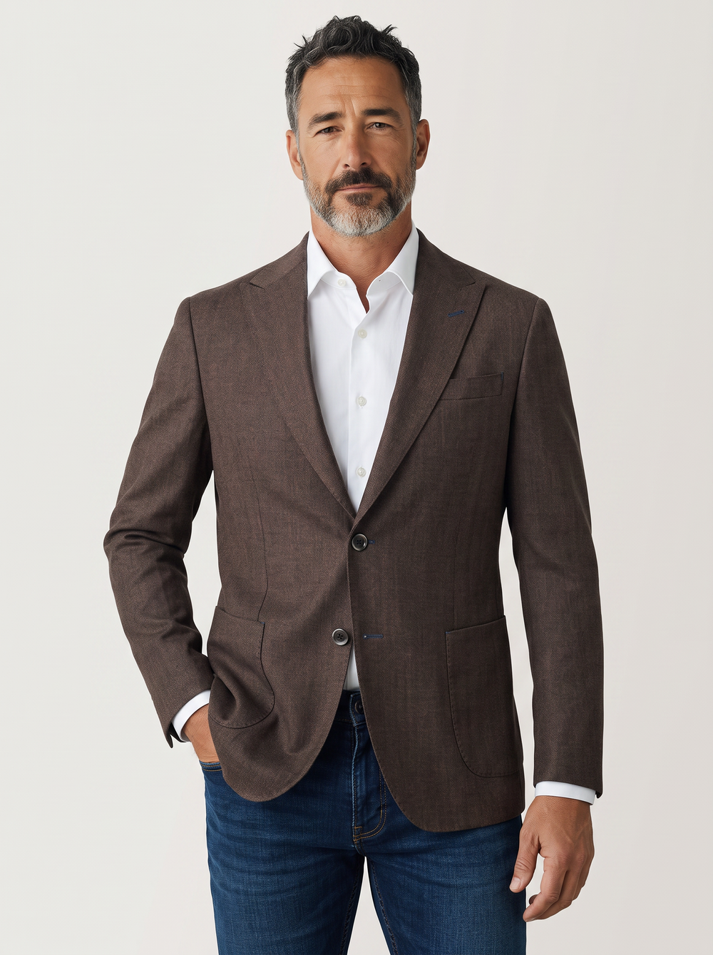 A man wearing a brown textured blazer over a white dress shirt and blue jeans.
