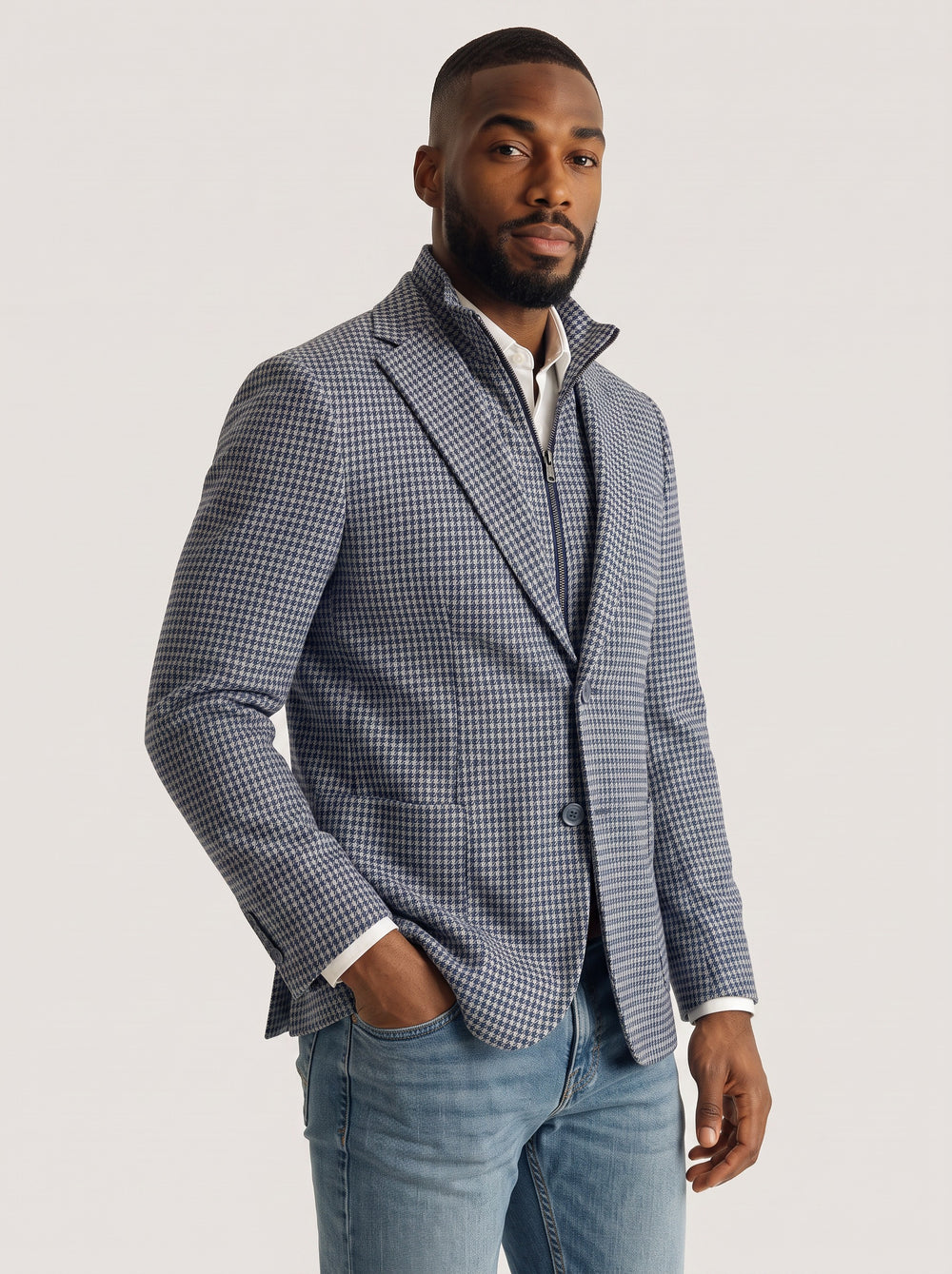 A man wearing a blue and white checkered blazer over a white shirt and blue jeans