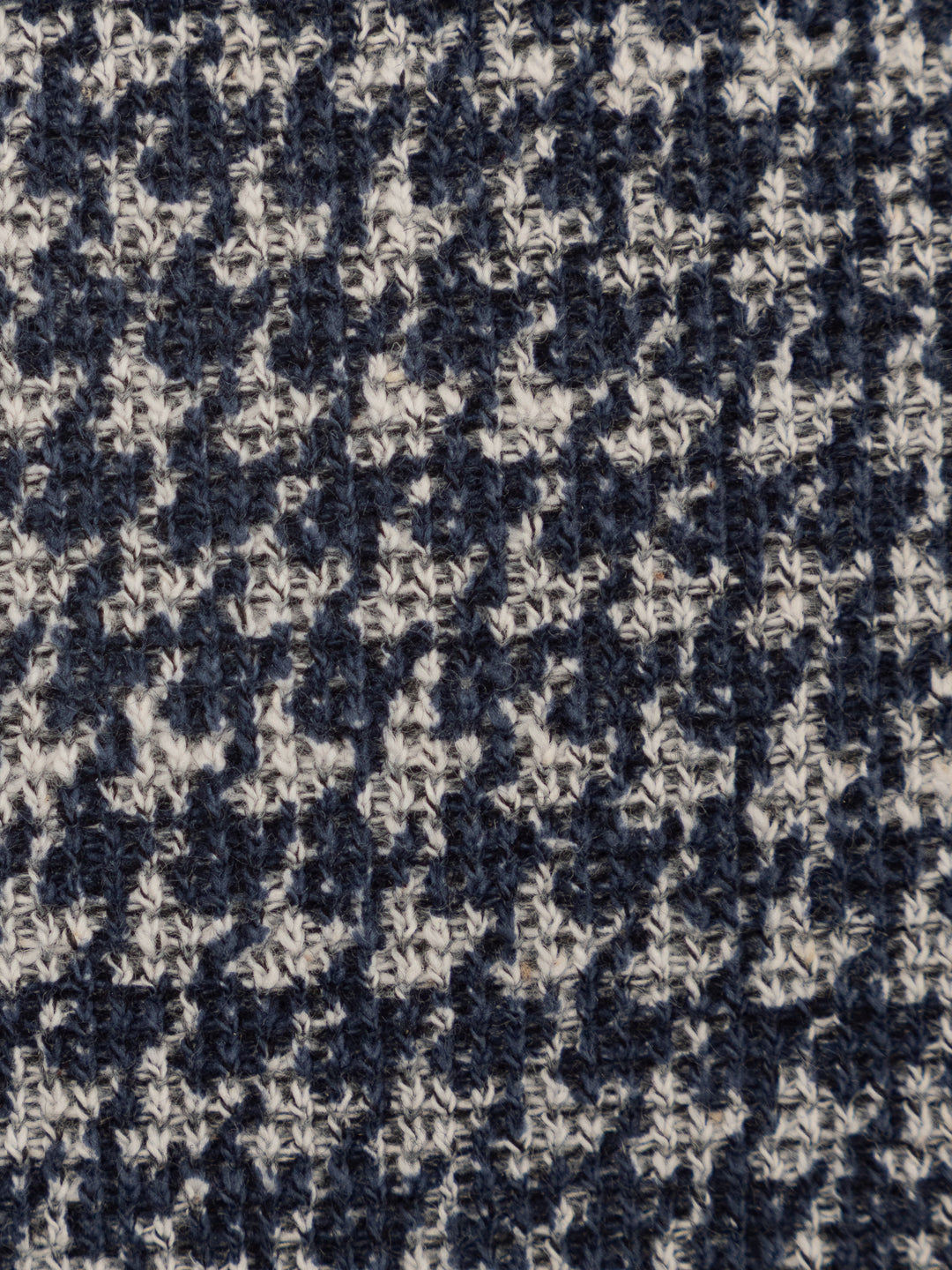 Close-up of a textured knit fabric with a navy blue and off-white houndstooth pattern.