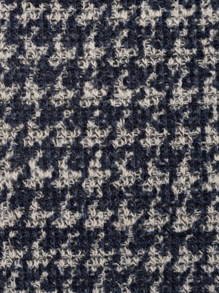 Close-up of a textured knit fabric with a navy blue and off-white houndstooth pattern.