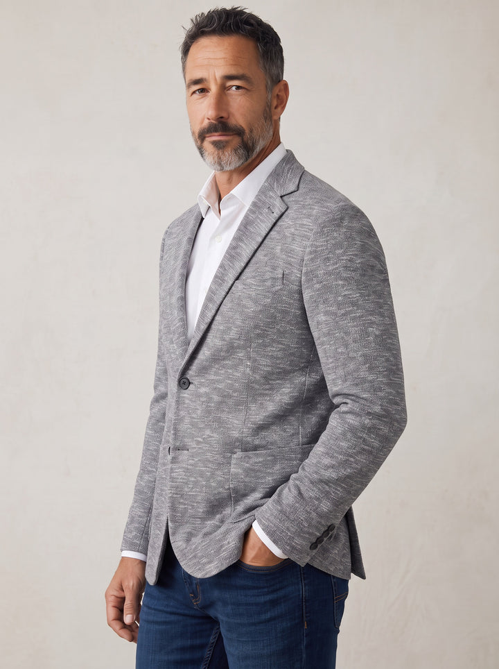 A man wearing a light gray heathered blazer over a white collared shirt and dark blue jeans