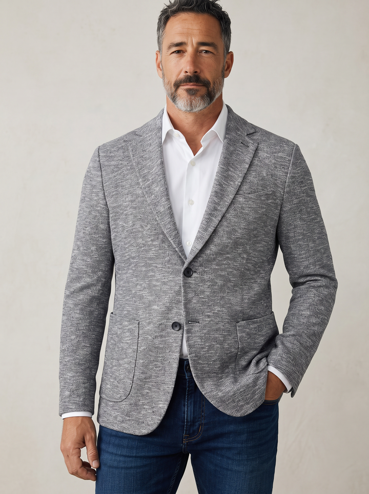 A man wearing a heather gray blazer over a white dress shirt and blue jeans