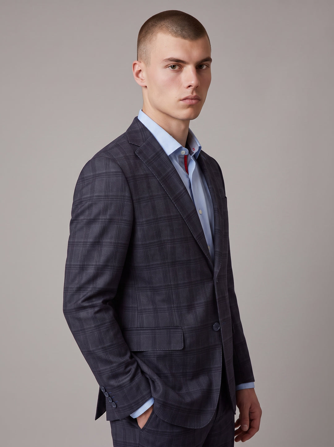 A man wearing a dark navy blue plaid suit jacket over a light blue dress shirt 