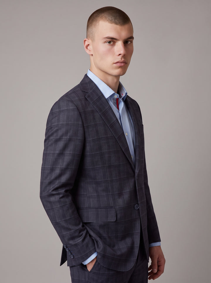 A man wearing a dark navy blue plaid suit jacket over a light blue dress shirt 