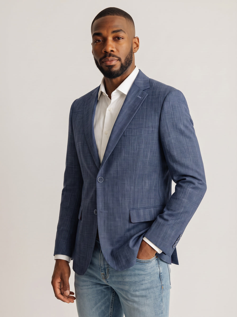A man wearing a blue textured blazer over a white collared shirt and light blue jeans