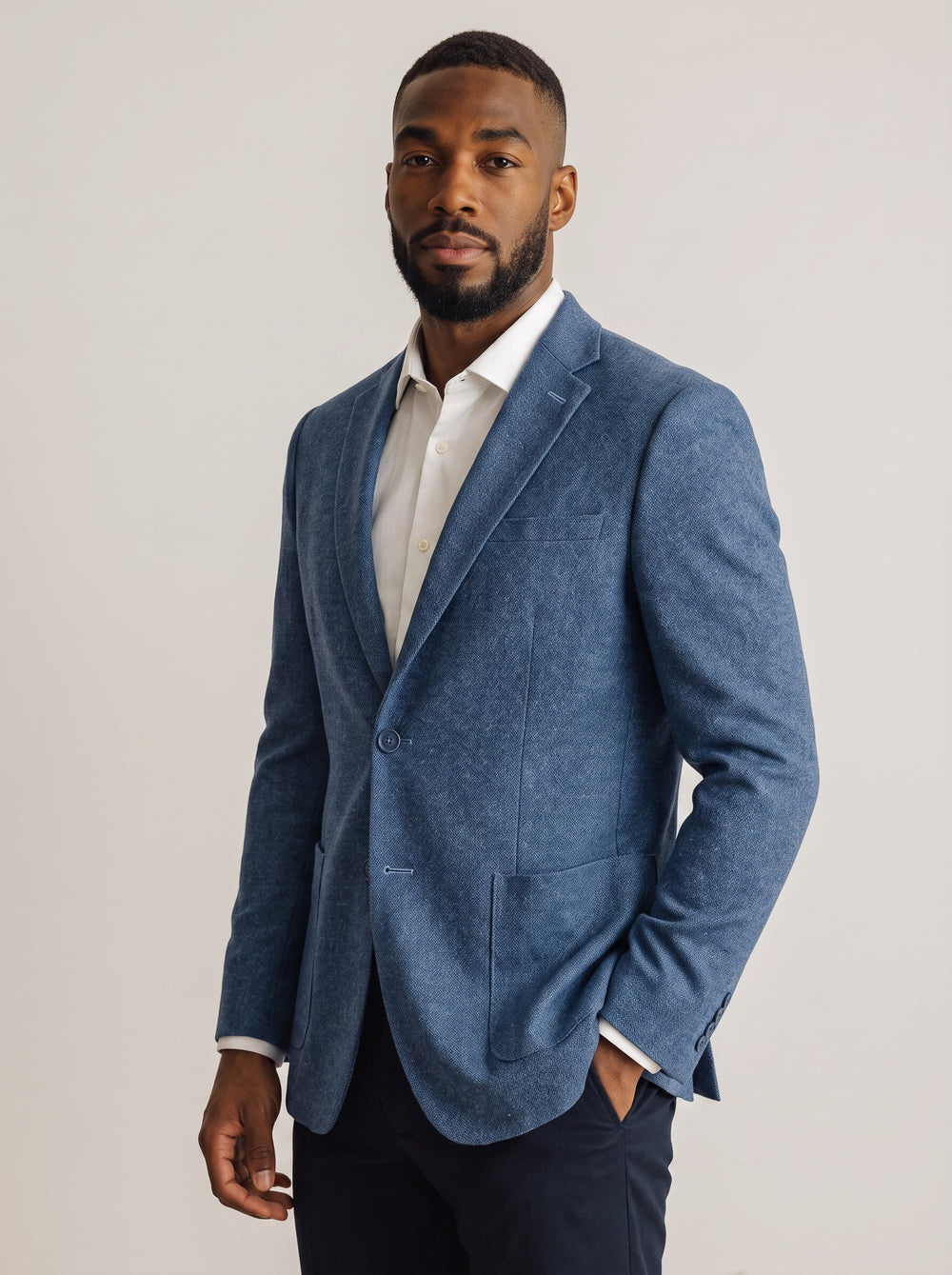 A man wearing a textured blue blazer over a white collared shirt and dark trousers