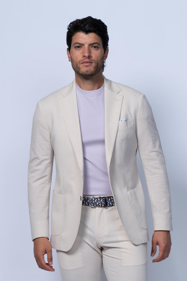 Man wearing a light-colored suit with a white shirt and patterned belt against a light background