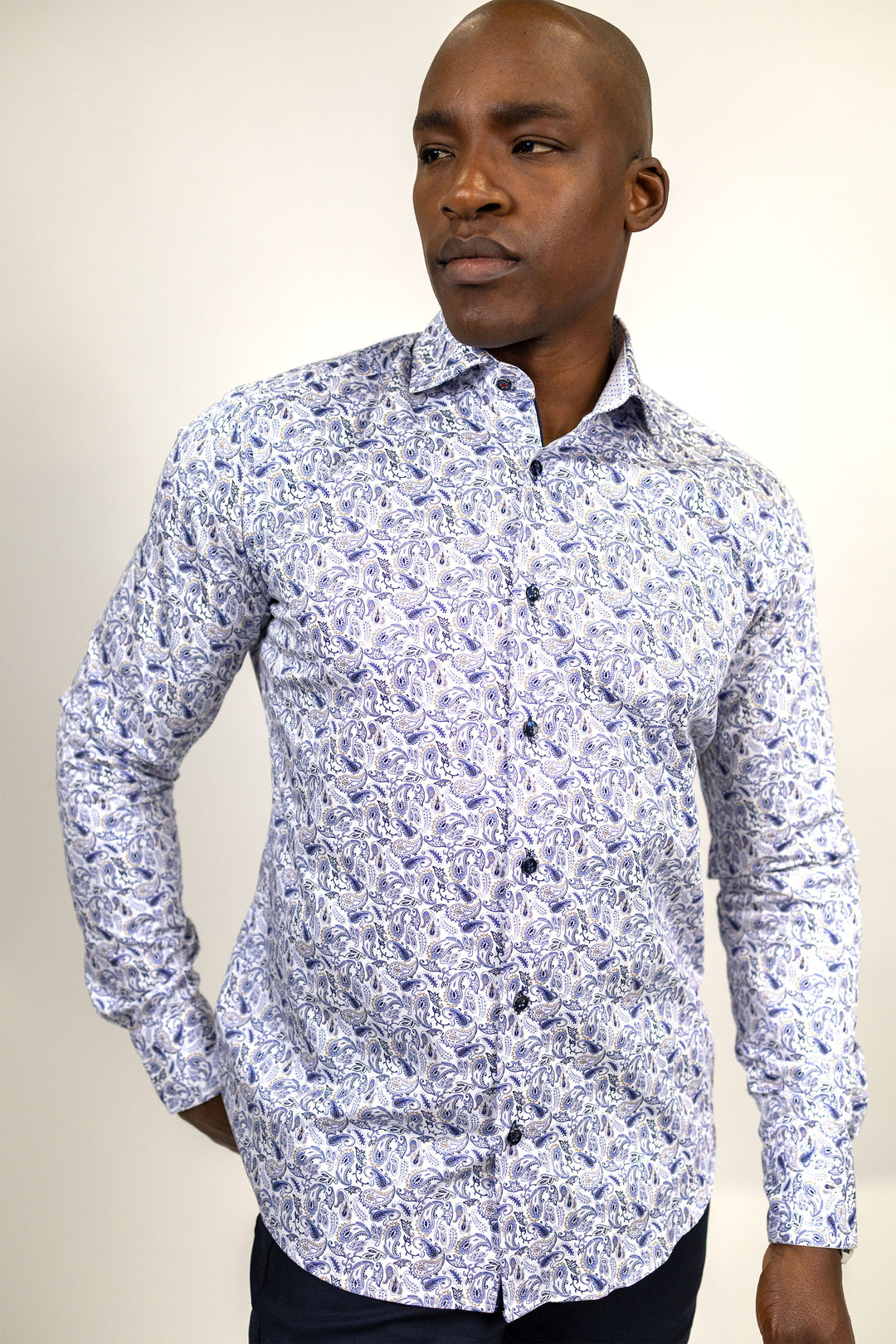 A man wearing a long-sleeve button-up shirt with a dense blue and white abstract floral pattern, photographed against a plain light beige studio background.