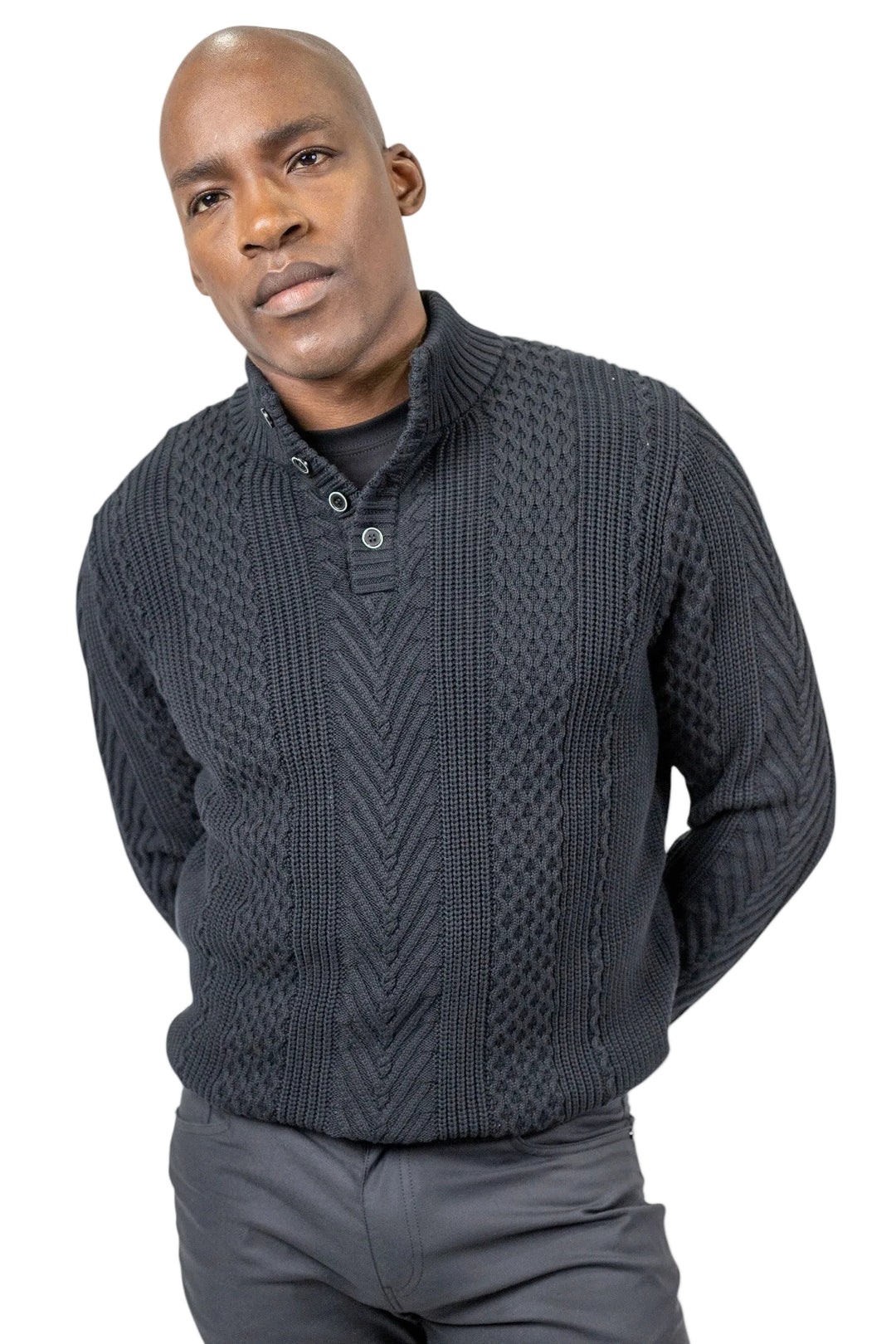 A man wearing a dark charcoal gray cable-knit mock neck sweater with a three-button placket, paired with gray trousers, against a plain white background.