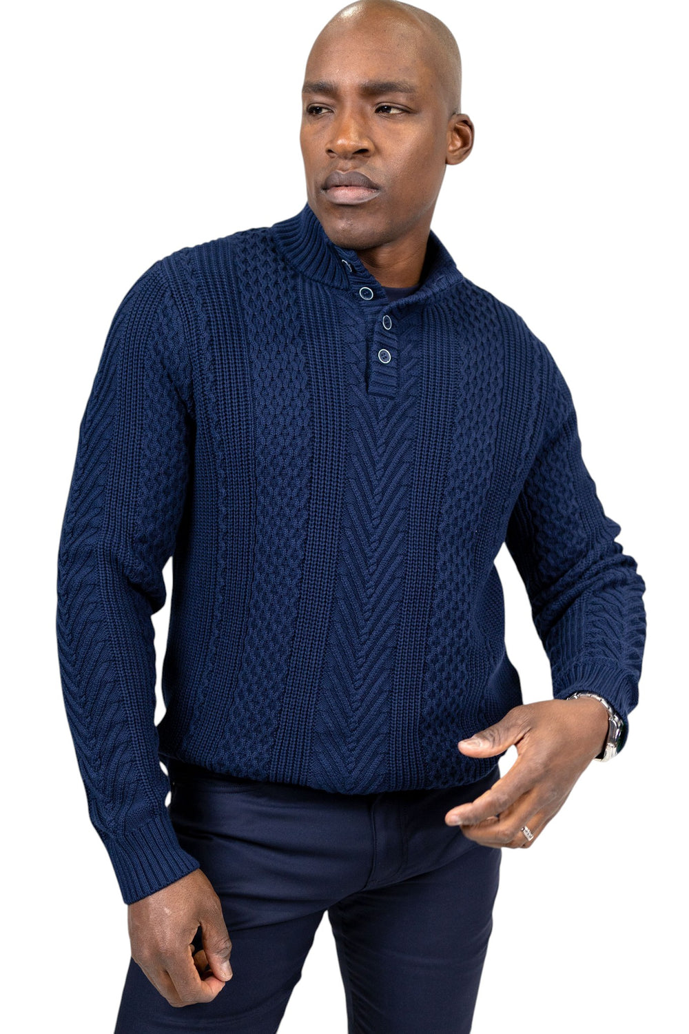 A man wearing a navy blue cable-knit mock-neck sweater with a three-button placket, paired with dark trousers, against a plain white background.