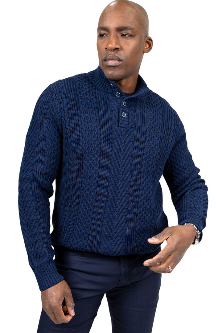 A man wearing a navy blue cable-knit mock-neck sweater with a three-button placket, paired with dark trousers, against a plain white background.